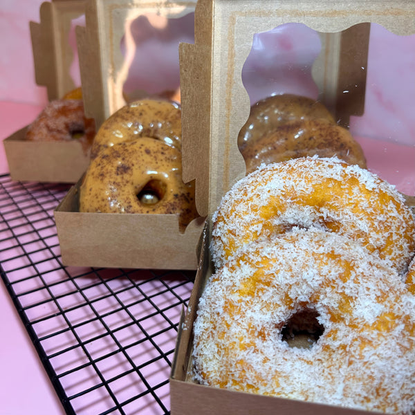 Argola Dourada de coco em caixa kraft, com os sabores doce de leite e clássica atrás